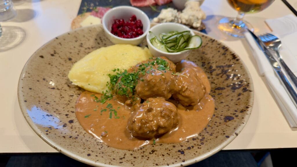 Meatballs in cream sauce with mashed potatoes, raw stir-fried lingonberries and pickled cucumber